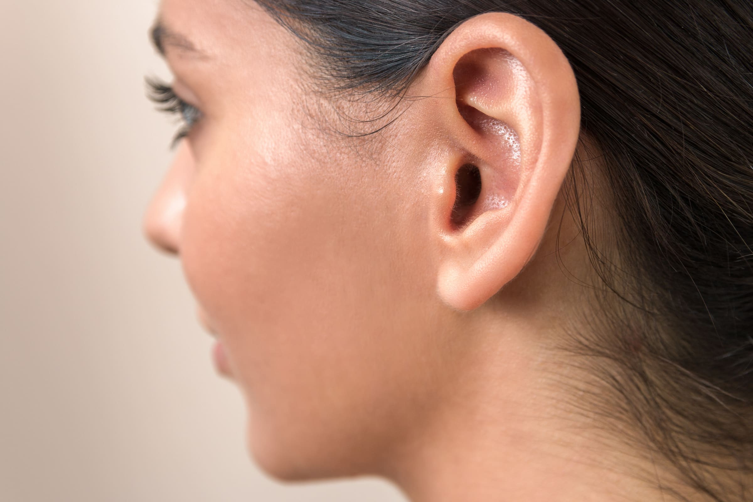Profile of a woman with her dark hair pulled back, showing her ear against a soft beige background
