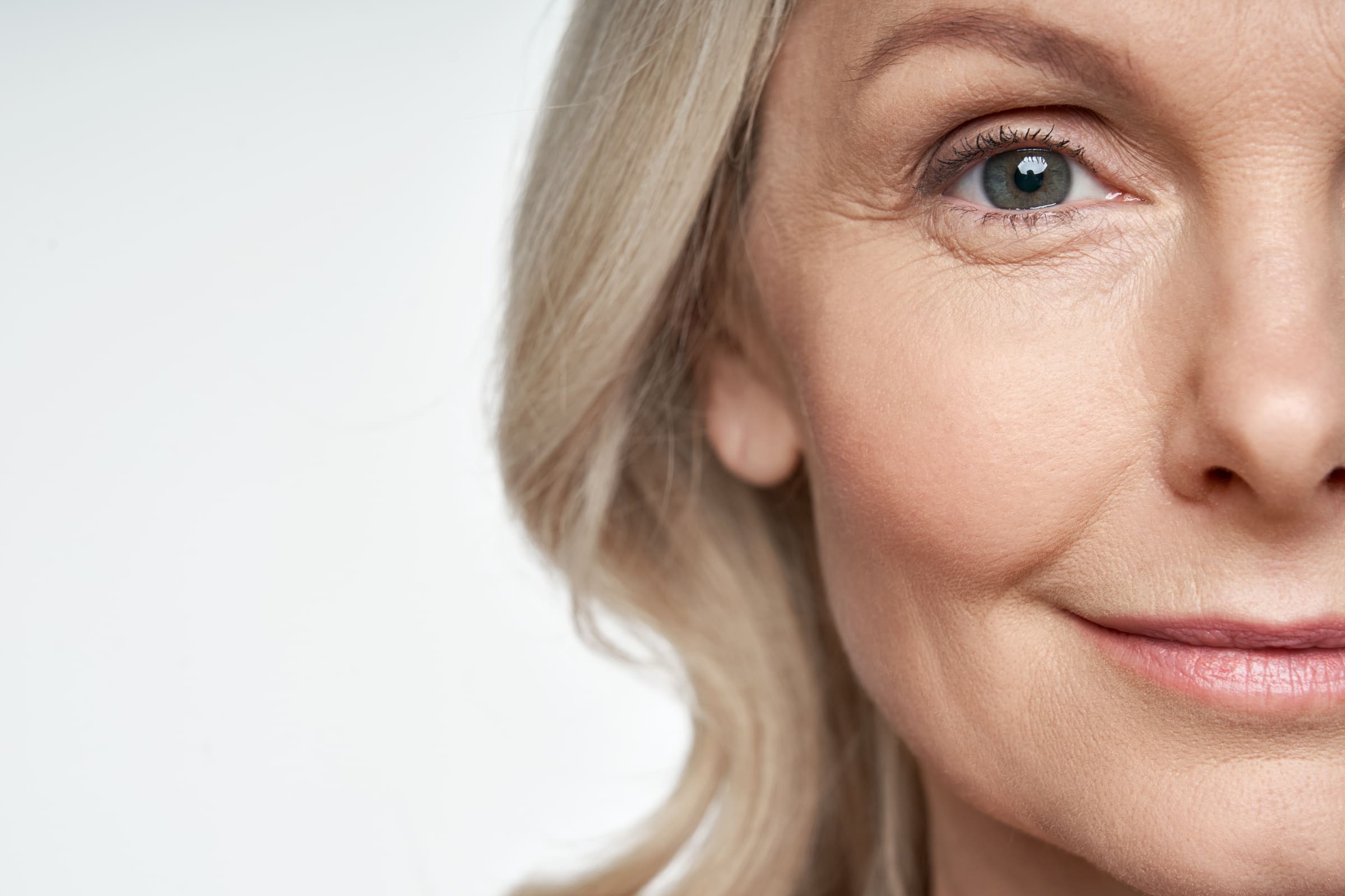 Close up of a mature woman’s eye and cheek, smiling softly, with blonde hair framing her face