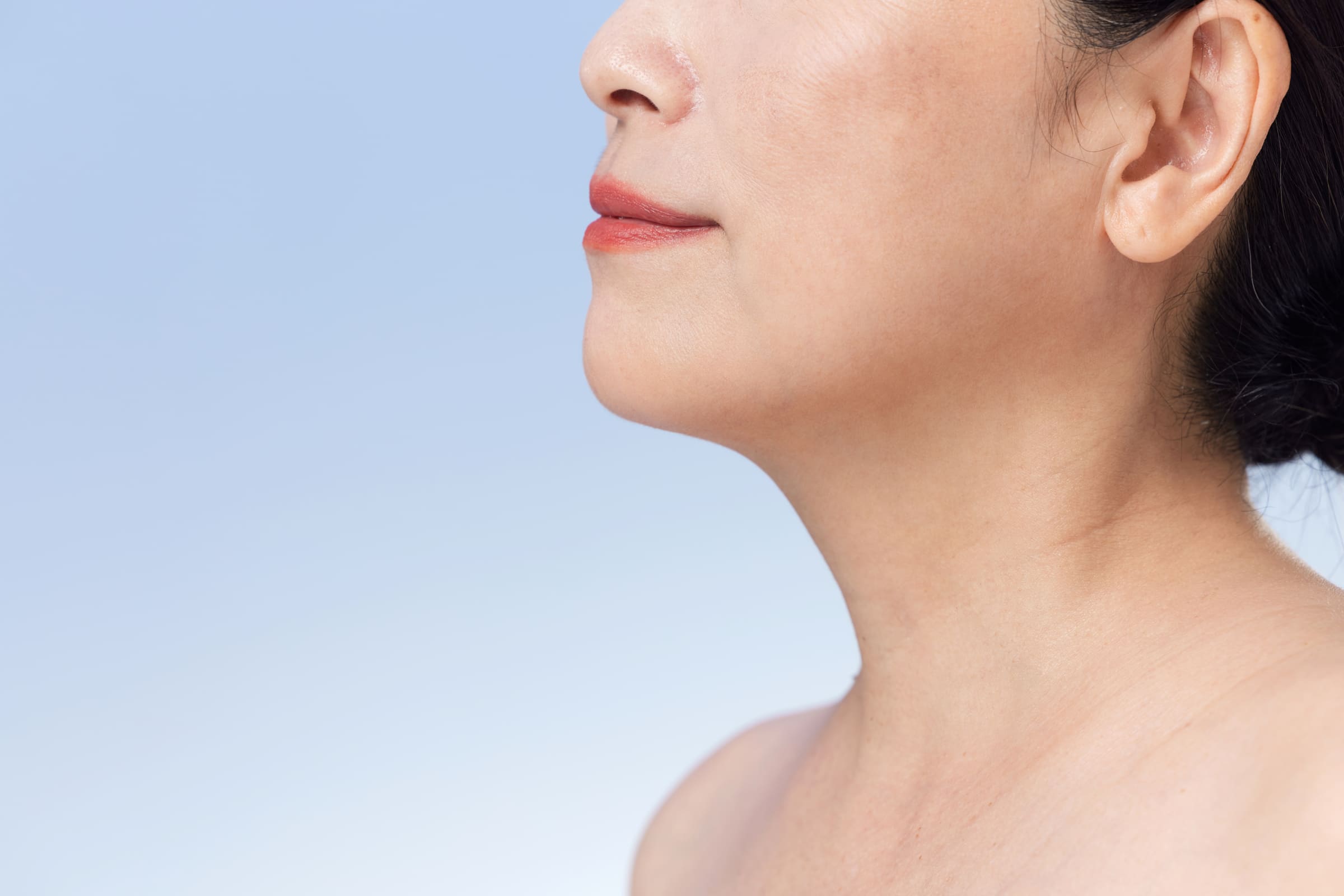 Profile of a woman’s jawline and neck against a pale blue sky