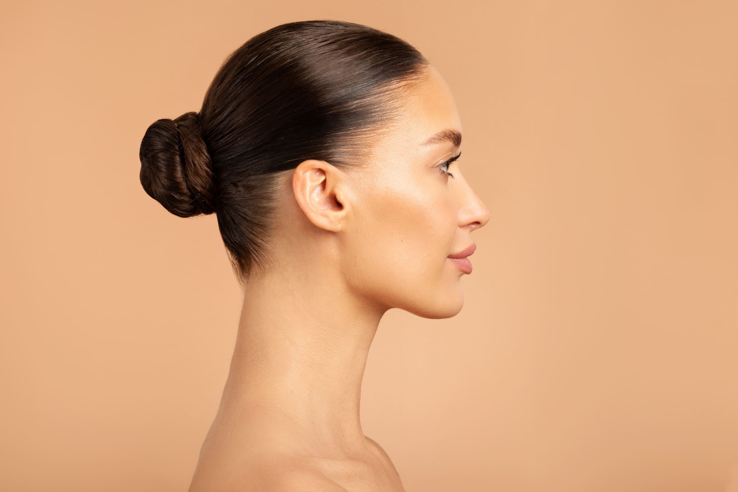 Profile of a woman with her hair in a low bun against a warm peach background